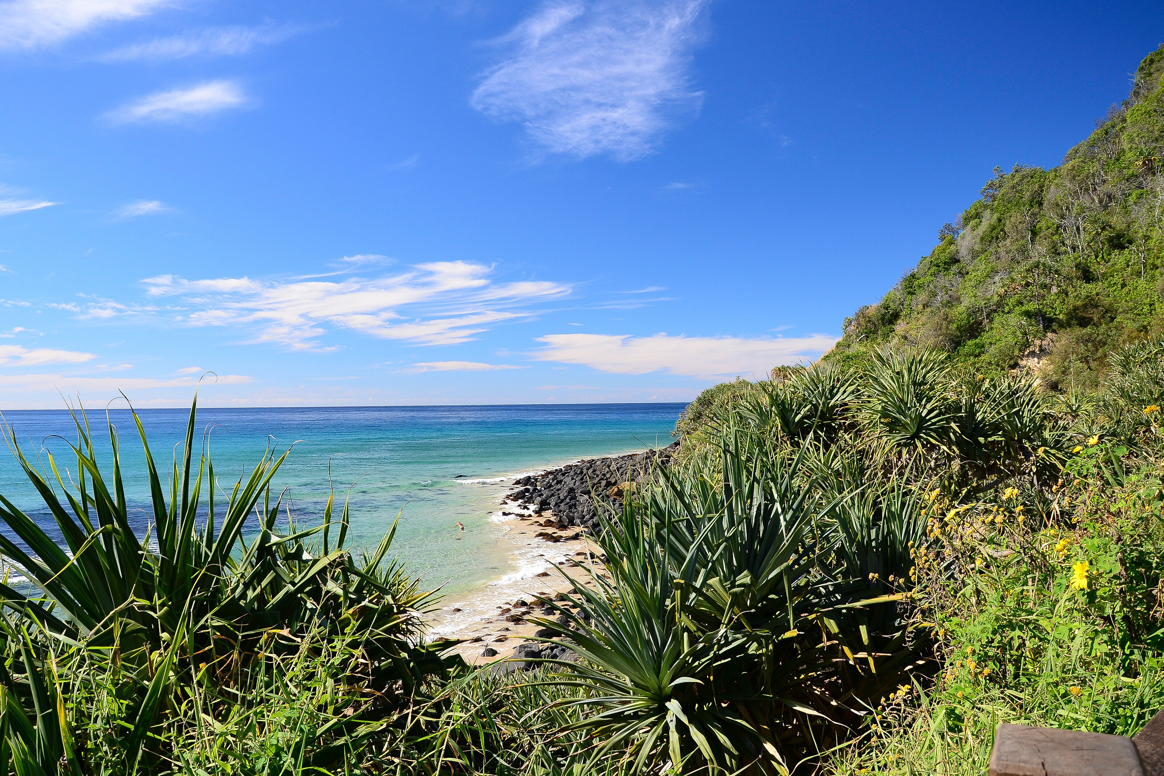 A coastal landscape with clear blue water, a sandy beach, and lush greenery.