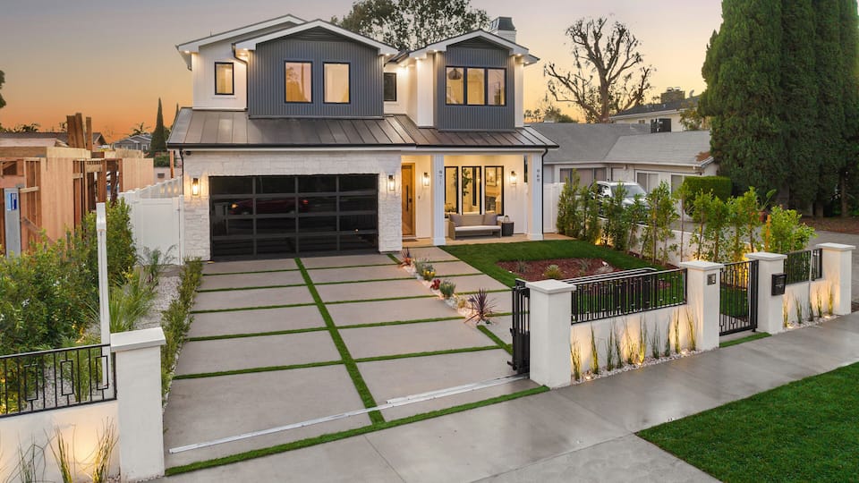 A modern two-story house with a garage, a well-maintained lawn, and a gated driveway.
