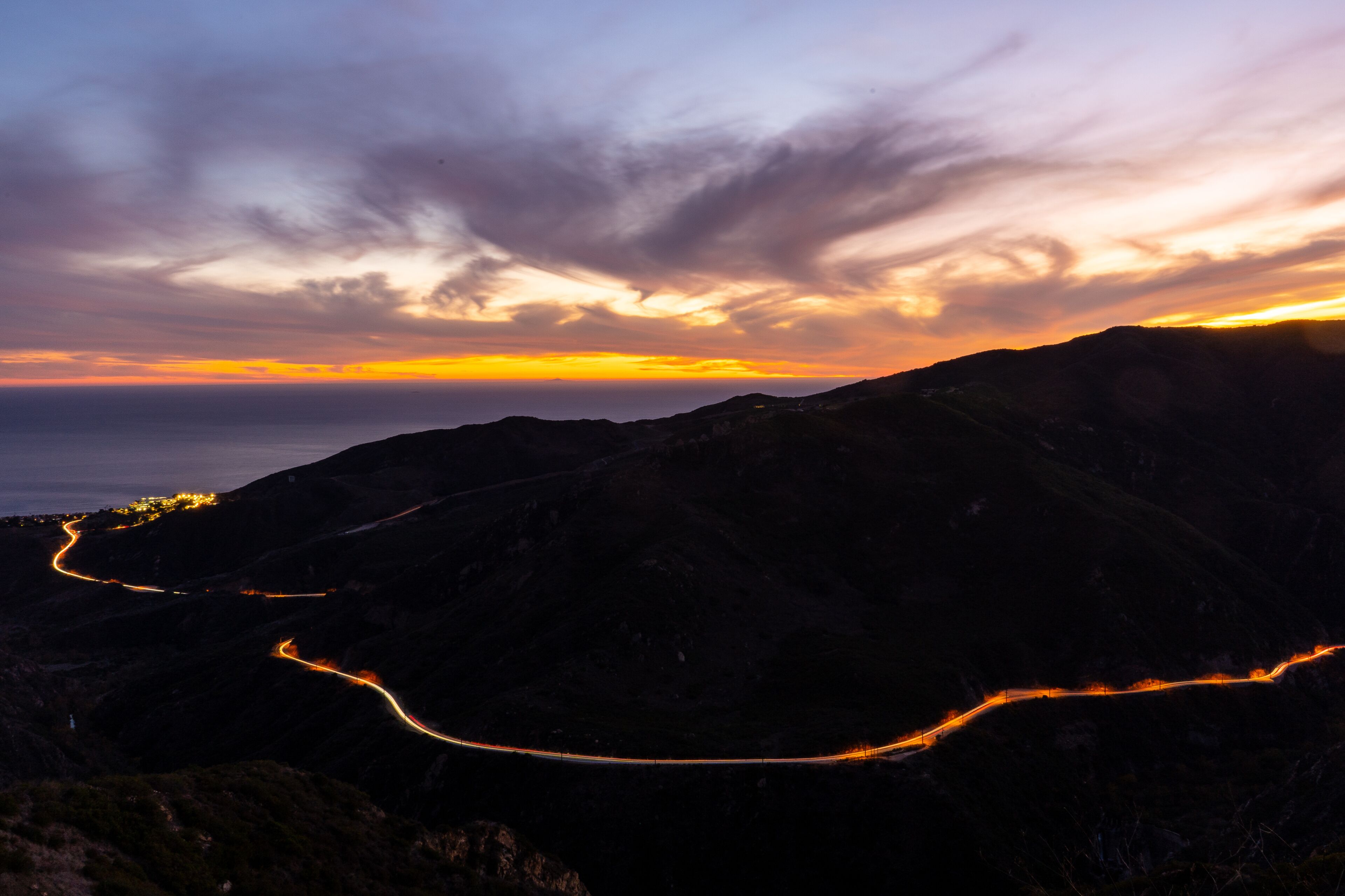 Sun setting horizon and mountains. Photo taken from a lookout in the Santa Monica mountains in Malibu. Headlights and taillights of cars in traffic are seen on the meandering and scenic PCH