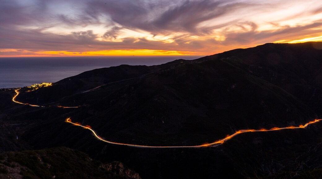 Sun setting horizon and mountains. Photo taken from a lookout in the Santa Monica mountains in Malibu. Headlights and taillights of cars in traffic are seen on the meandering and scenic PCH