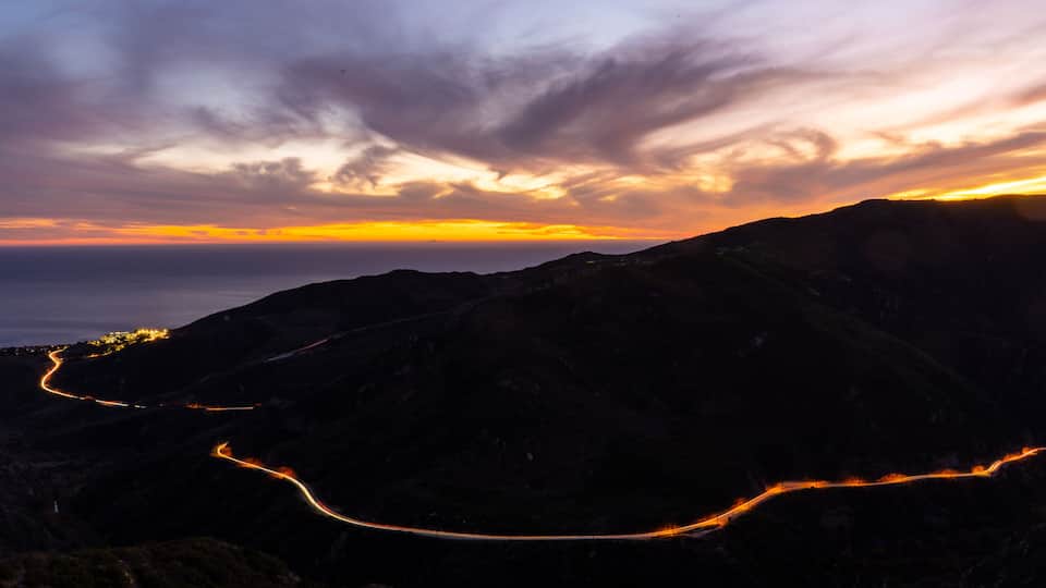 Sun setting horizon and mountains. Photo taken from a lookout in the Santa Monica mountains in Malibu. Headlights and taillights of cars in traffic are seen on the meandering and scenic PCH