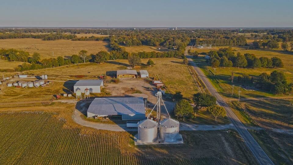 An aerial view of a rural farm with barns, silos, and a road.
