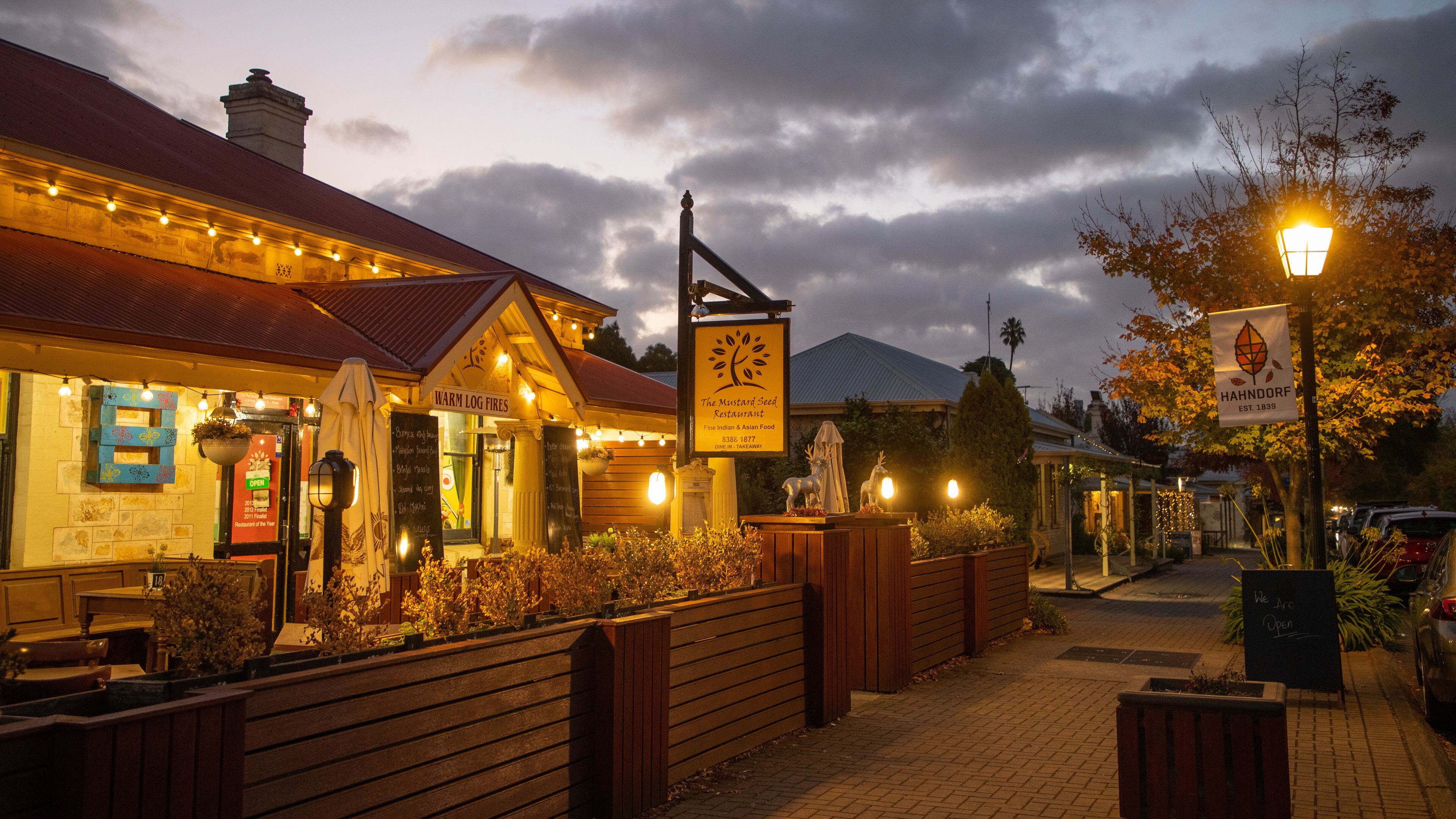 A cozy restaurant named "The Mustard Seed Restaurant" with a signboard and a warm log fire sign.