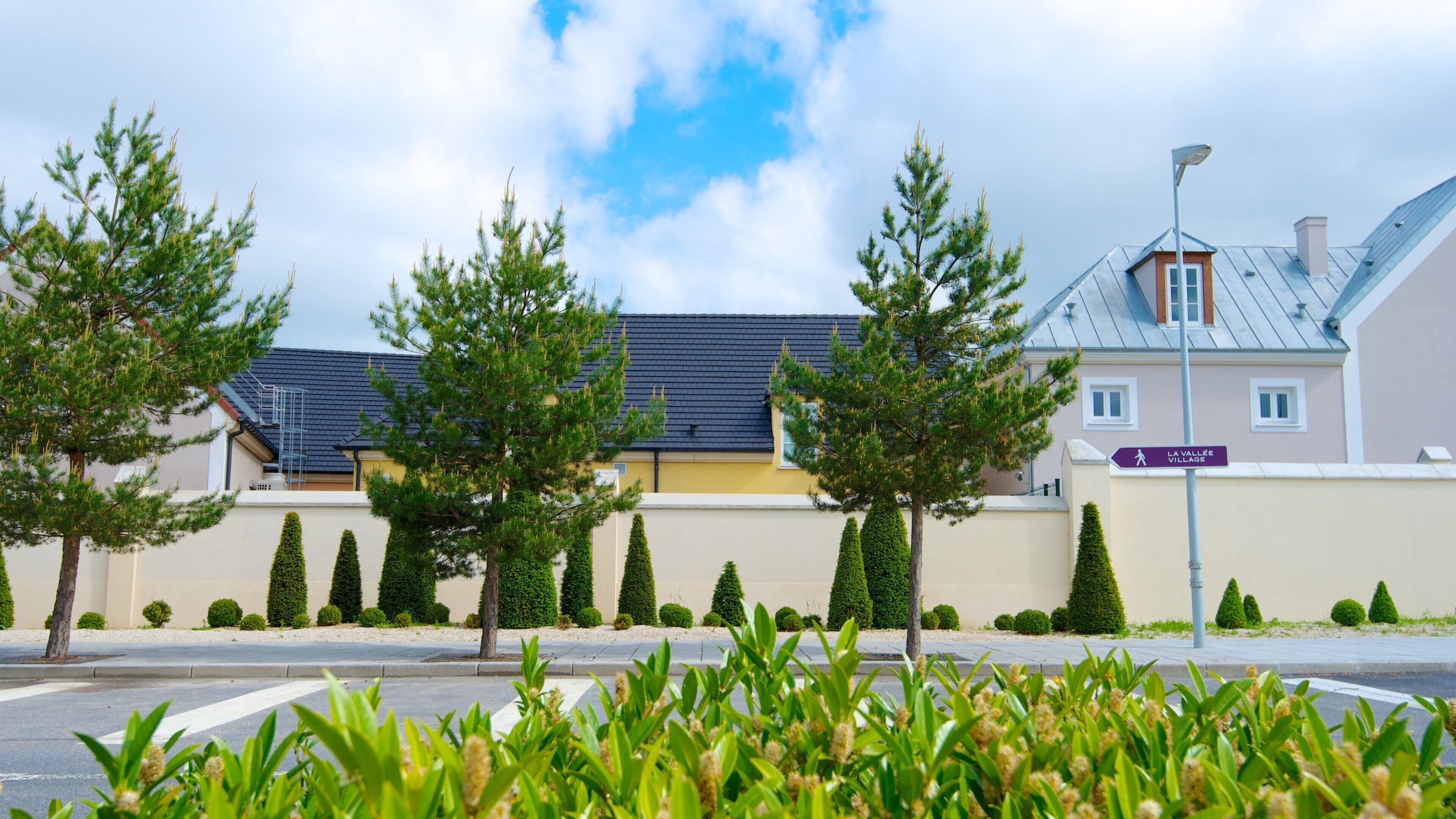 A street with neatly trimmed hedges, a crosswalk, and a sign for La Vallée Village.