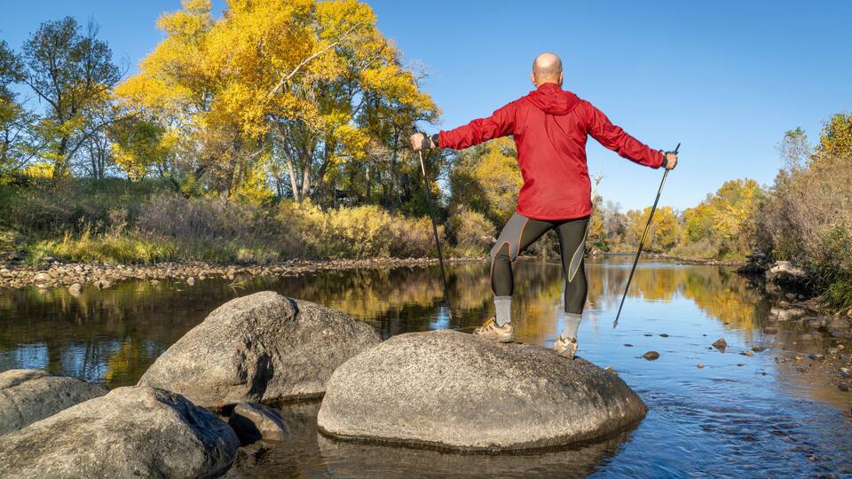 senior make hiker in his 70s with trekking poles on a shore of the Poudre River in Fort Collins, Colorado, fall scenery