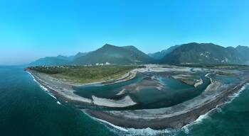 Luchtbeeld van een kustlandschap met een baai, een brug en een bergketen.