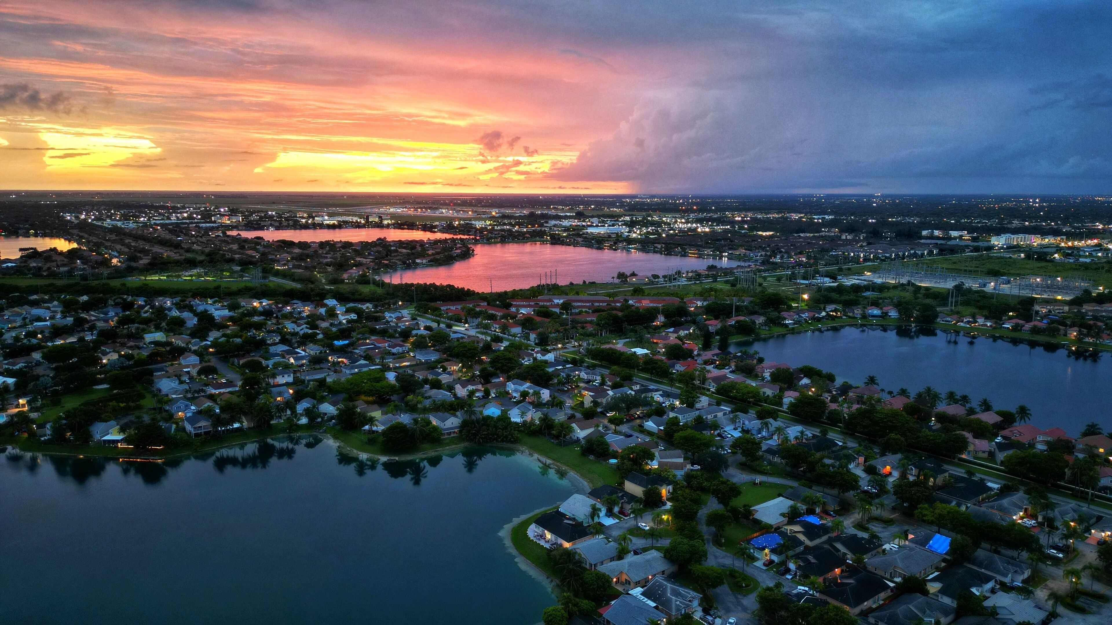 A coastal town at sunset with a large body of water, residential areas, and a distant city skyline.