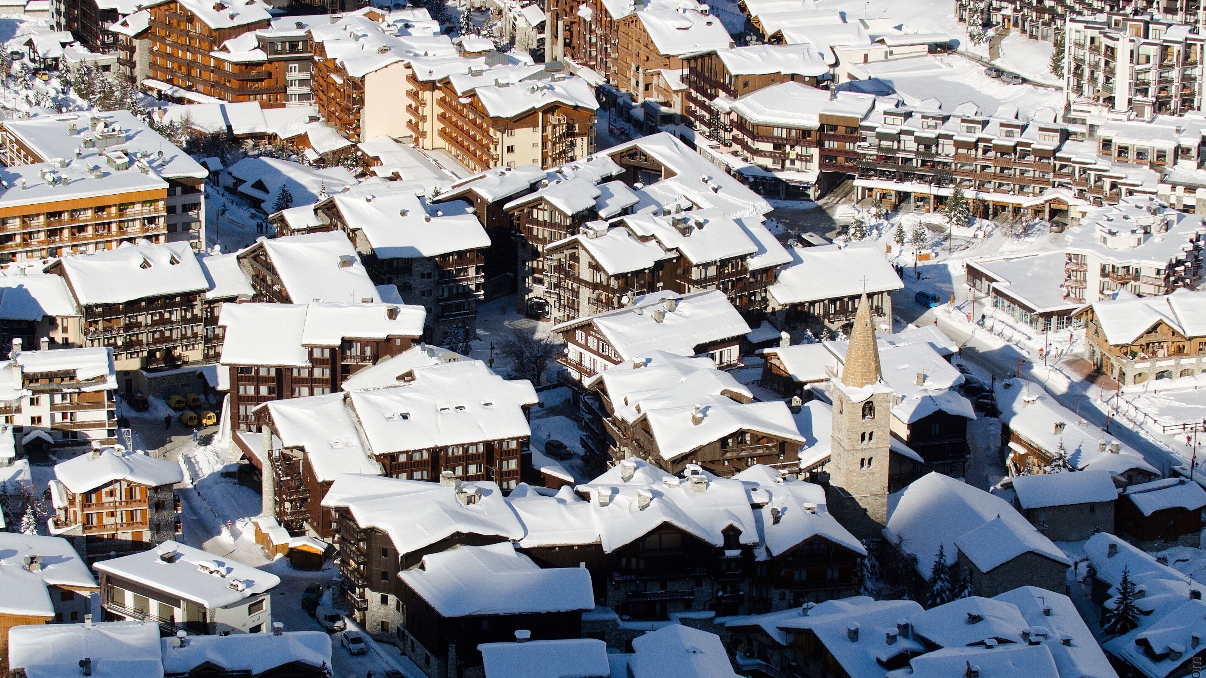A snow-covered village with traditional wooden buildings and a prominent church tower.