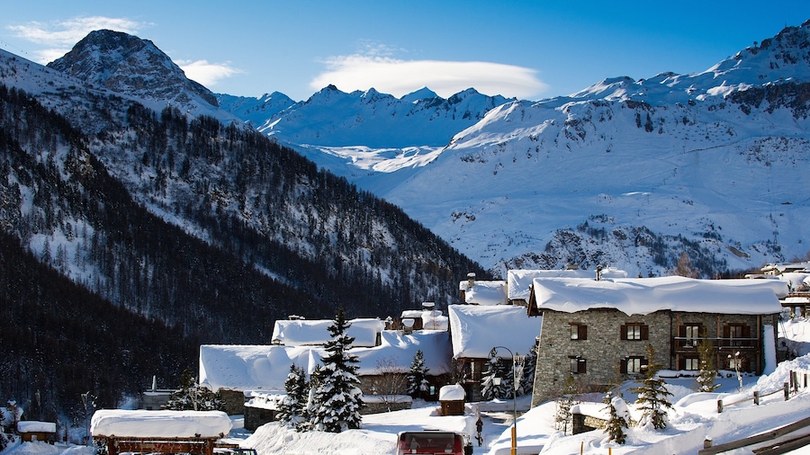 A snow-covered mountain village with stone buildings and a ski lift.