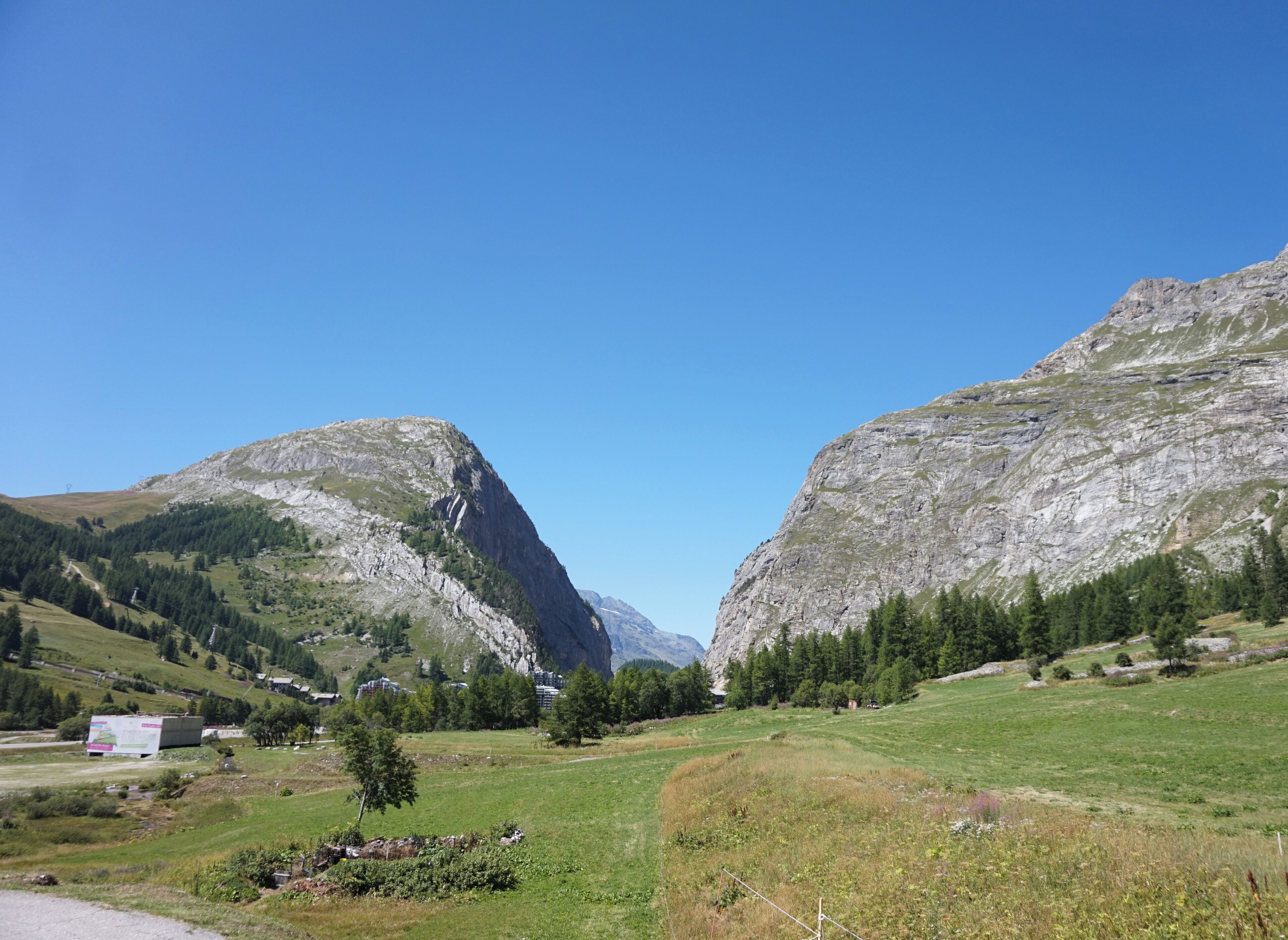 A mountainous landscape with a clear sky, a valley with scattered trees, and a few buildings.