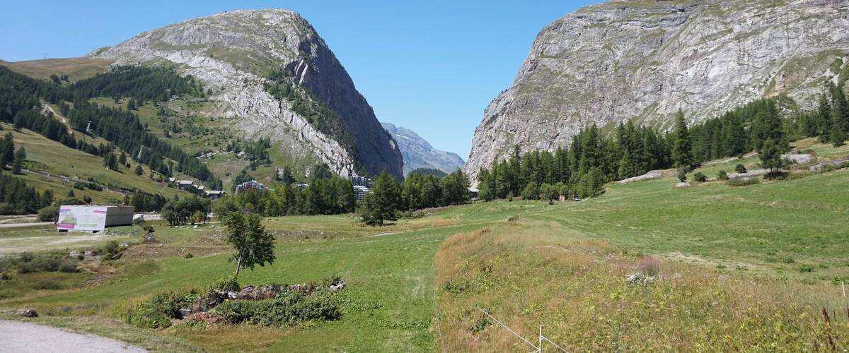 A mountainous landscape with a clear sky, a valley with scattered trees, and a few buildings.