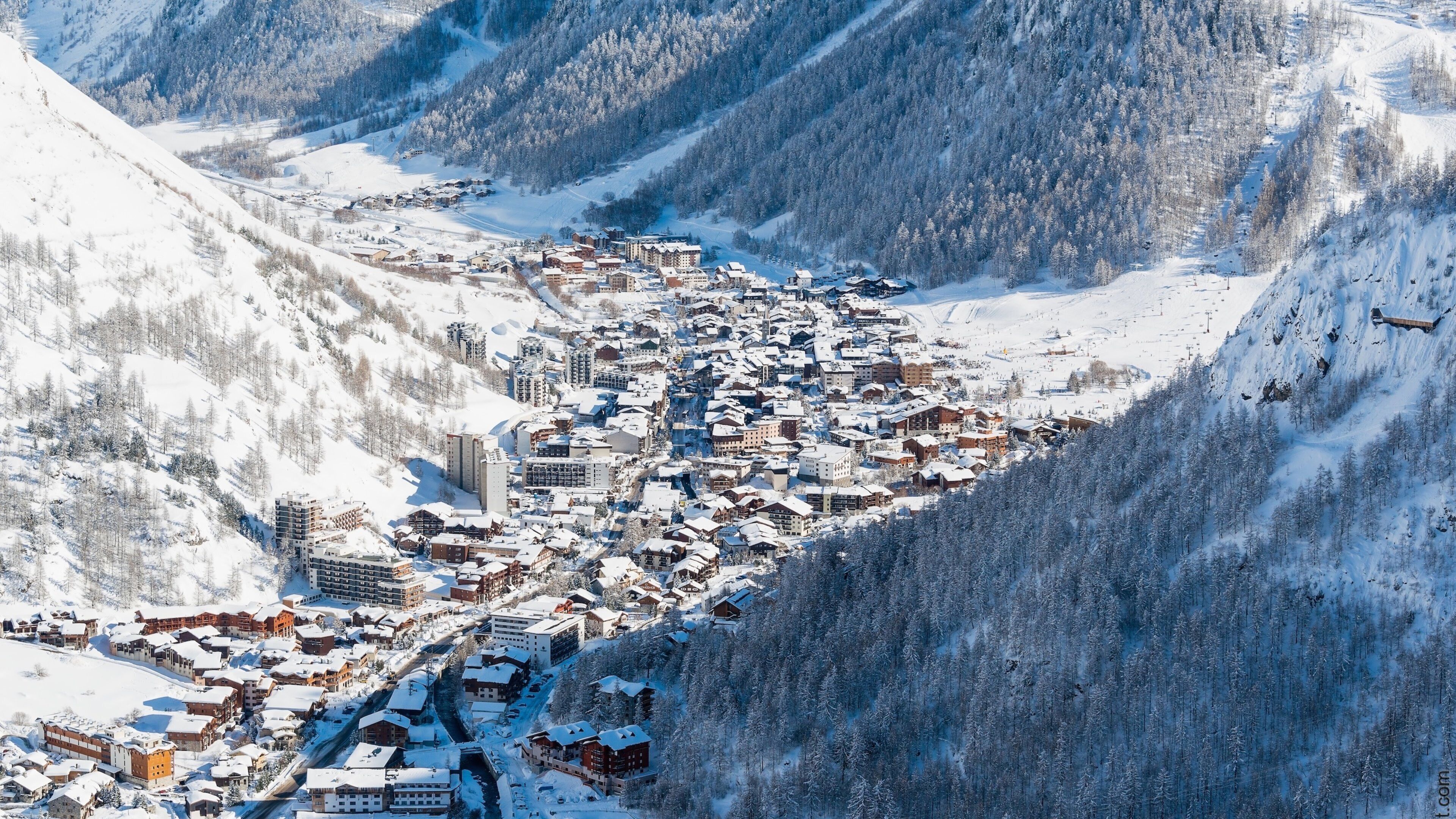 A snow-covered mountain town nestled in a valley with dense forests and steep slopes.