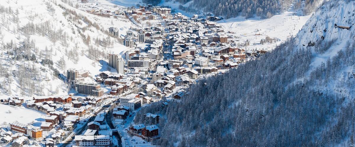 A snow-covered mountain town nestled in a valley with dense forests and steep slopes.