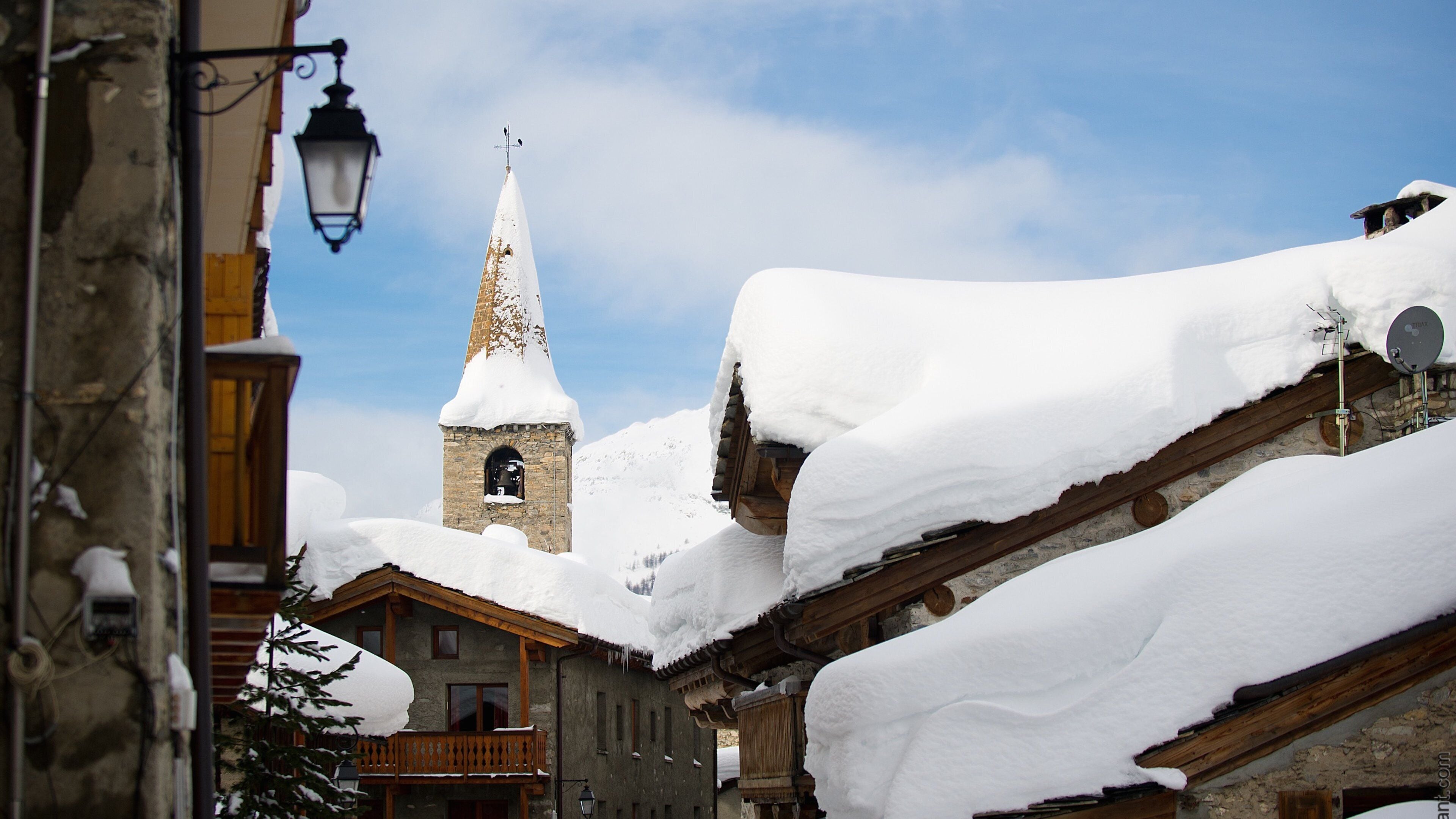 A snow-covered village with a church tower and wooden buildings.