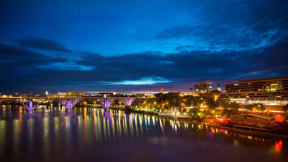 A nighttime cityscape with a bridge reflecting lights on a calm river.
