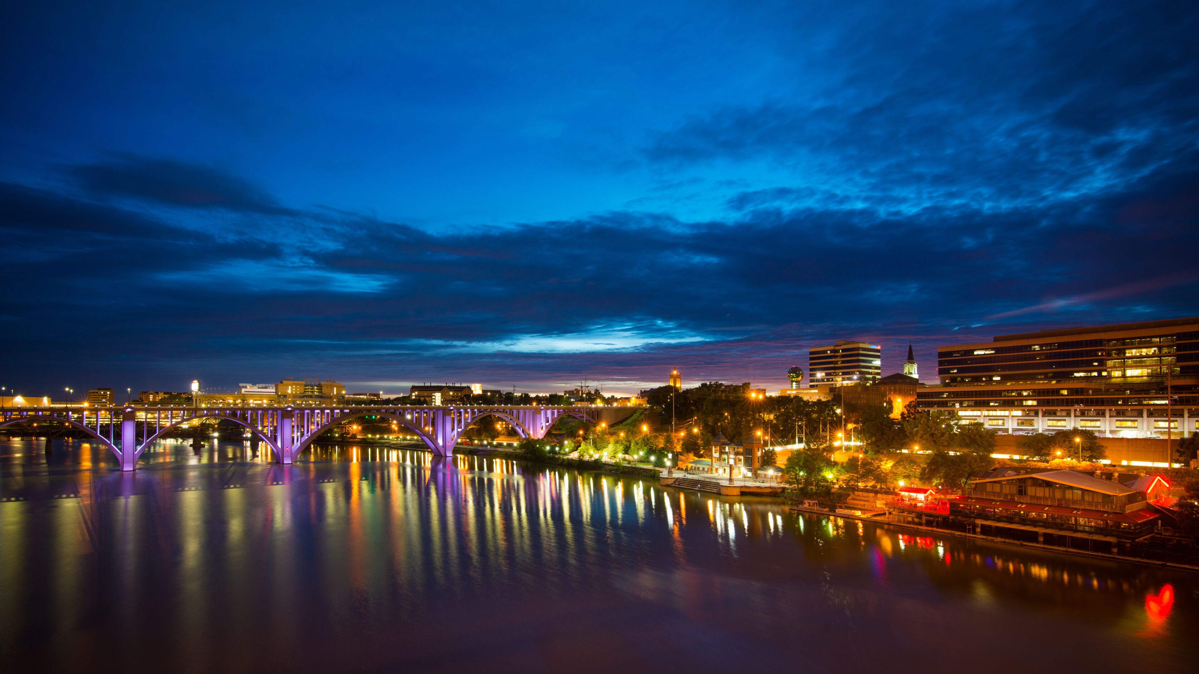 A nighttime cityscape with a bridge reflecting lights on a calm river.