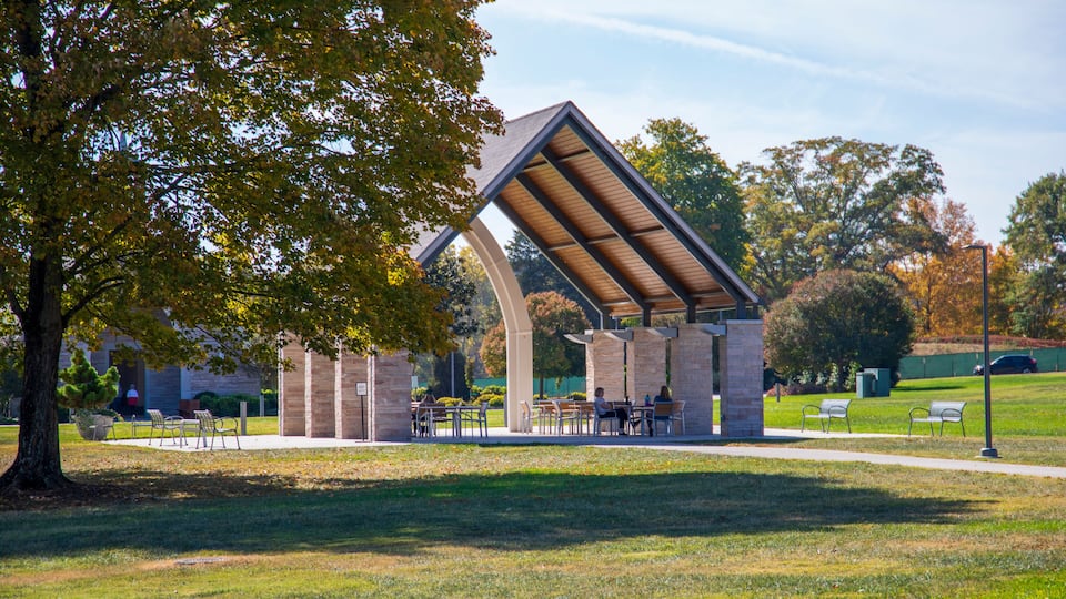 A park with a modern pavilion, benches, and a grassy area.