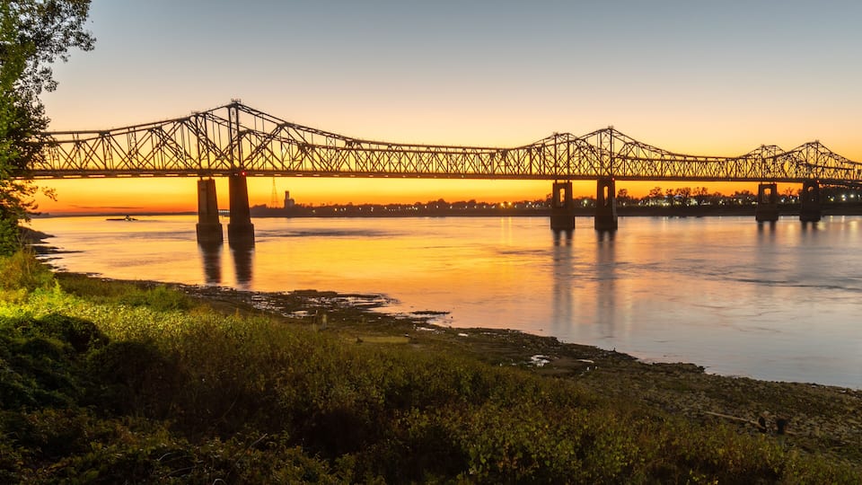 A bridge over a river at sunset with a city skyline in the background.