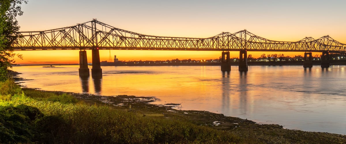 A bridge over a river at sunset with a city skyline in the background.