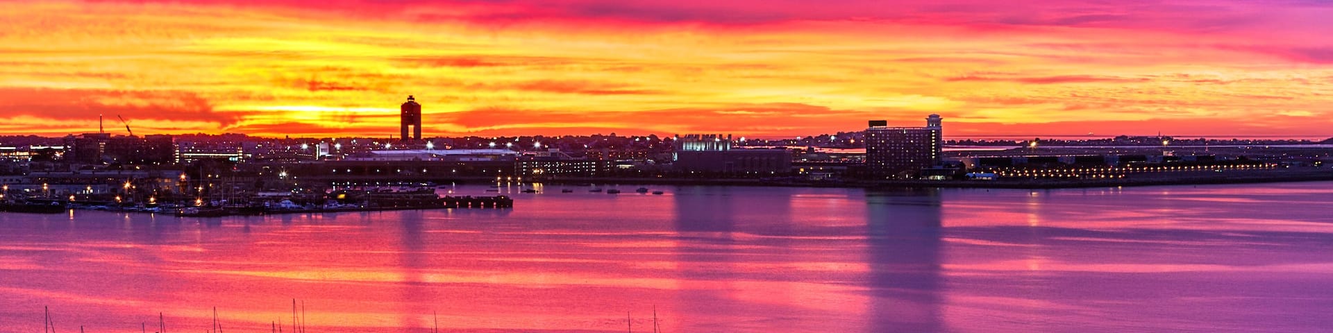 A sunset over a harbor with boats and buildings.