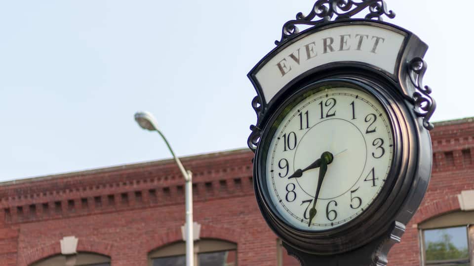 A clock with the name 'Everett' on it, set against a brick building.
