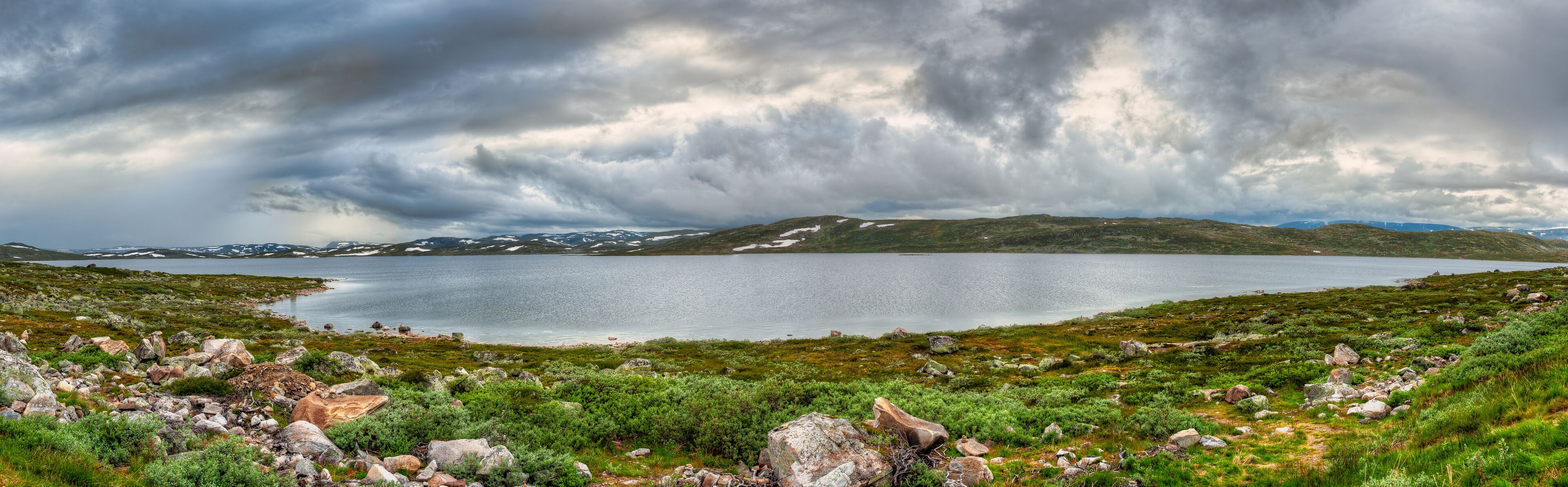 A lake surrounded by rocky terrain and sparse vegetation under a cloudy sky.