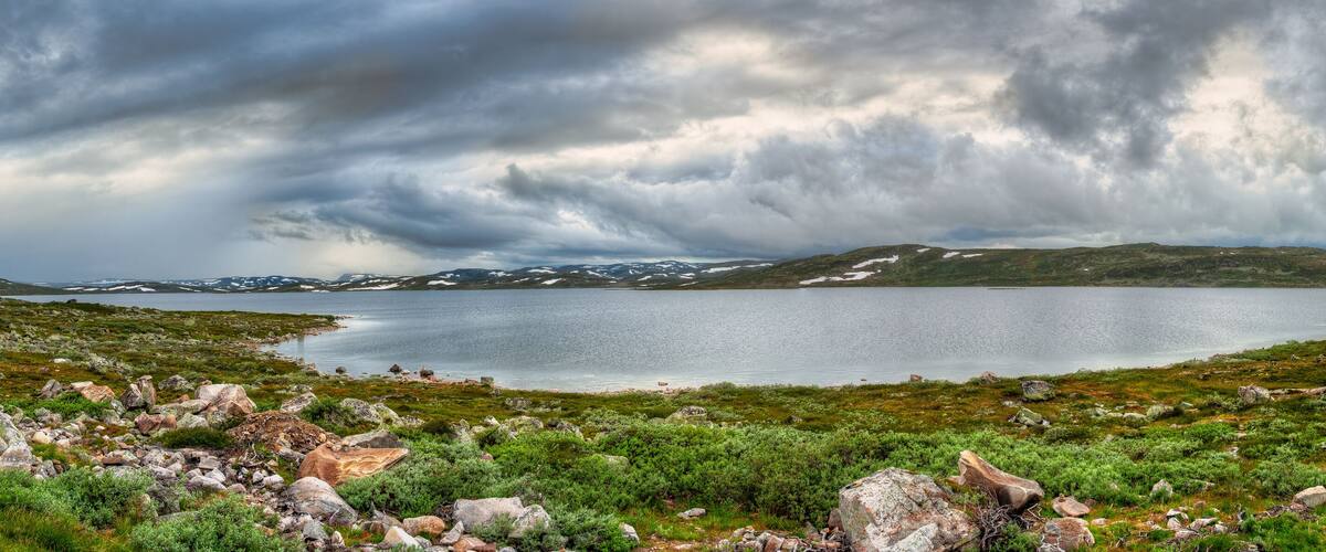 A lake surrounded by rocky terrain and sparse vegetation under a cloudy sky.