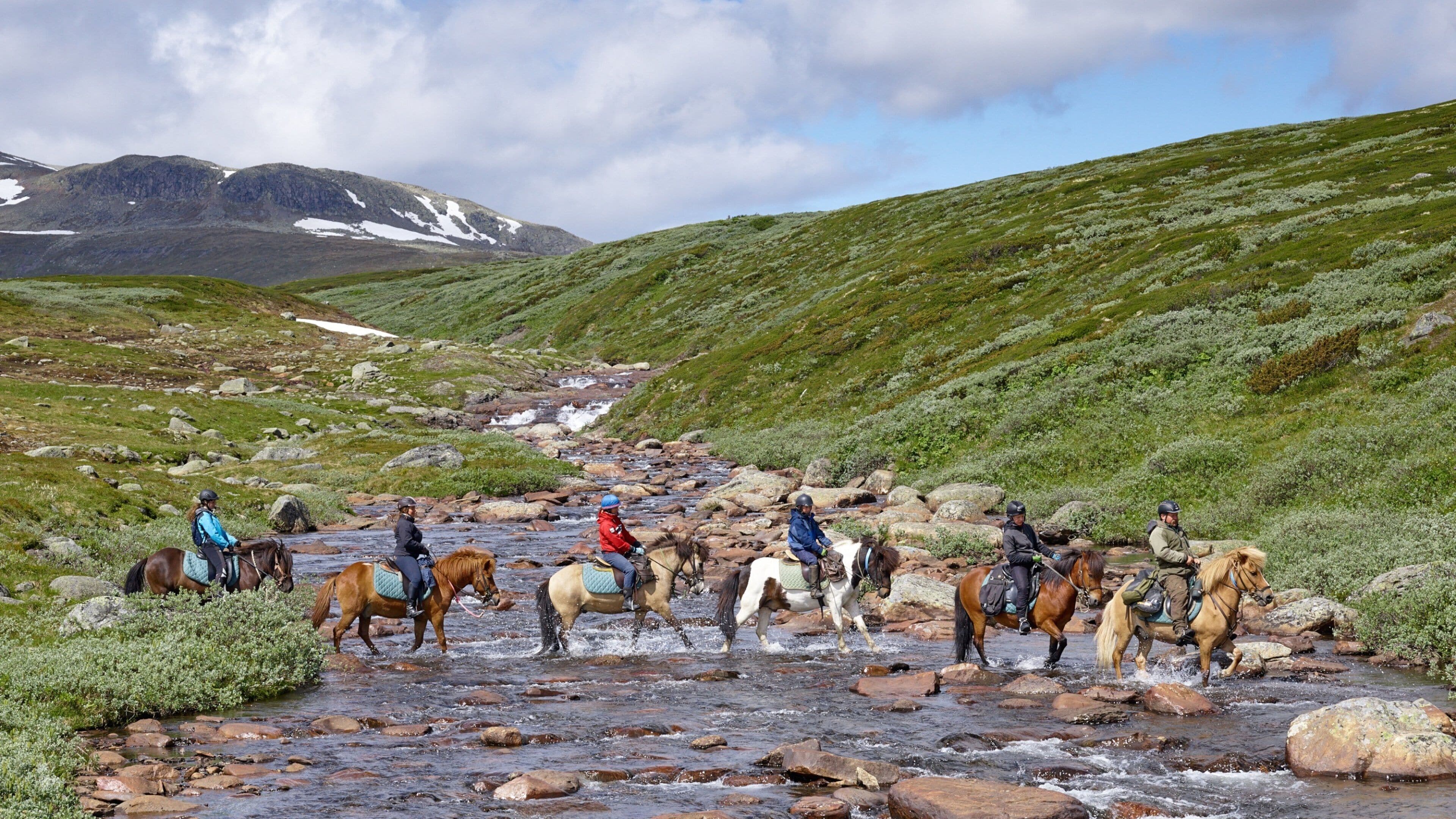 A group of people riding horses across a rocky stream in a mountainous area.