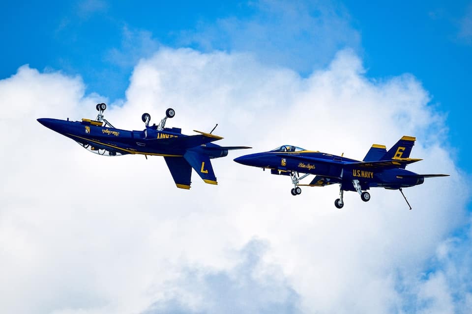 Dos aviones azules y amarillos volando en formación contra un cielo azul con nubes.