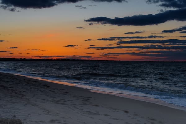 Une plage au coucher du soleil, avec des vagues qui déferlent sur le rivage et un ciel parsemé de nuages.