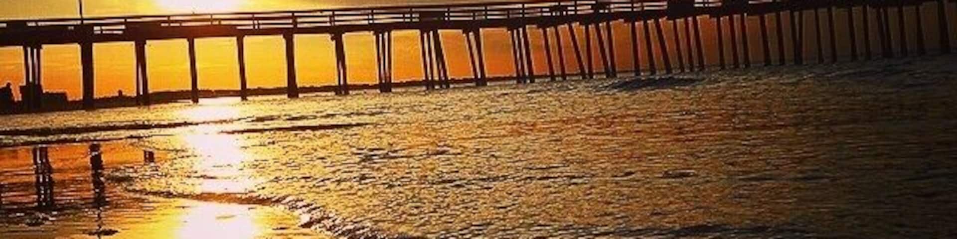 A sunset over a beach with a pier extending into the water.