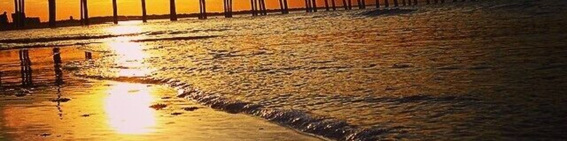 A sunset over a beach with a pier extending into the water.