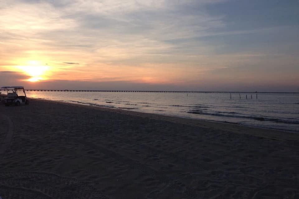 A beach at sunset with a pier extending into the water.