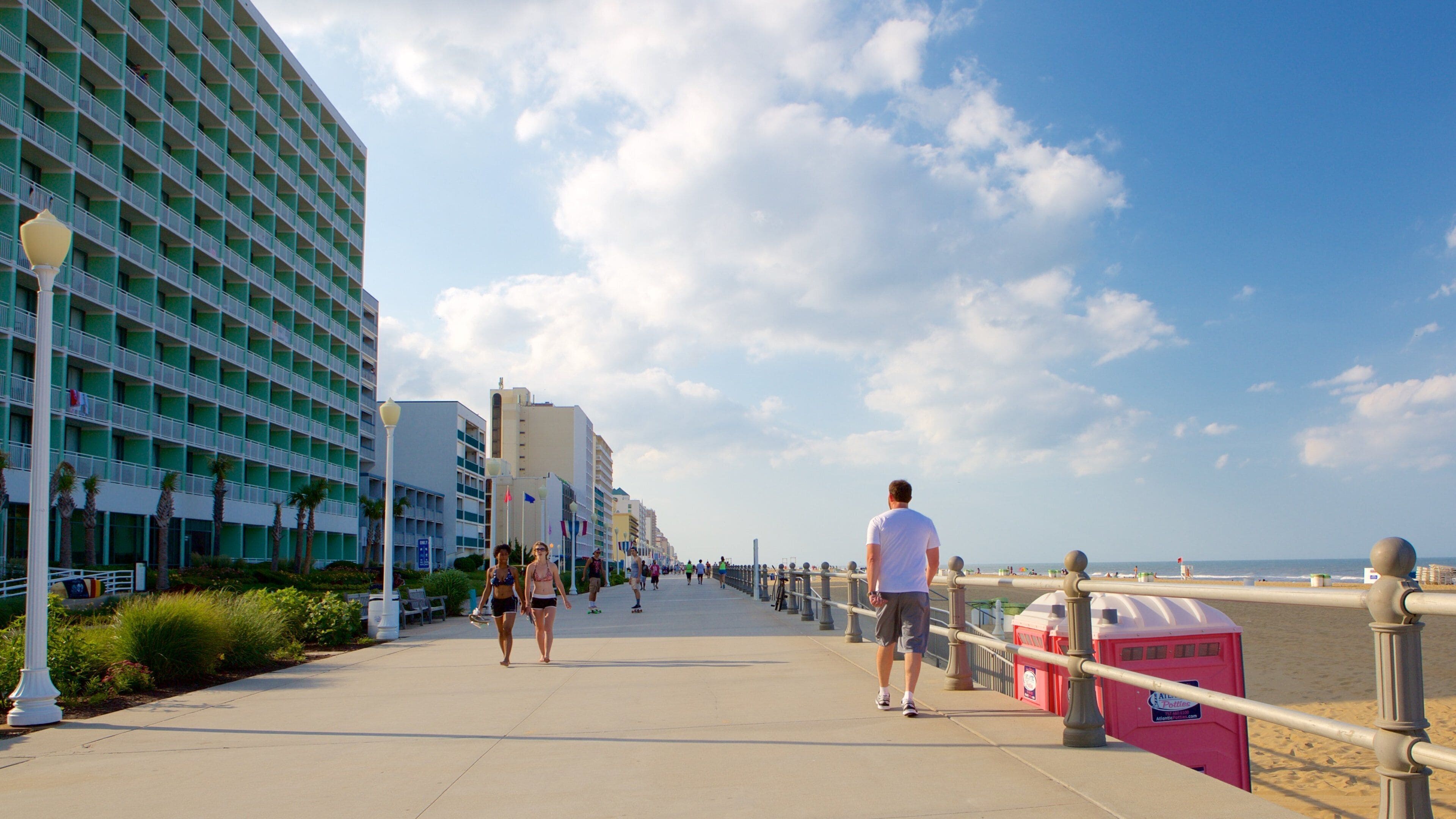 Eine Küstenpromenade mit Strand, einer Reihe von Hotels und blauem Himmel.