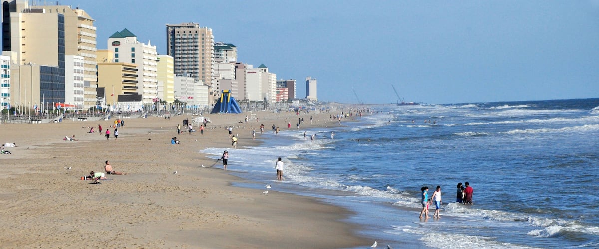 A sandy beach with waves, people, and buildings in the background.