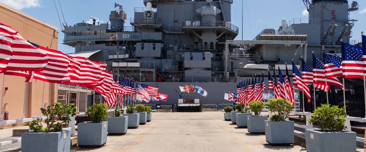 A naval shipyard with multiple American flags and potted plants lining the walkway.