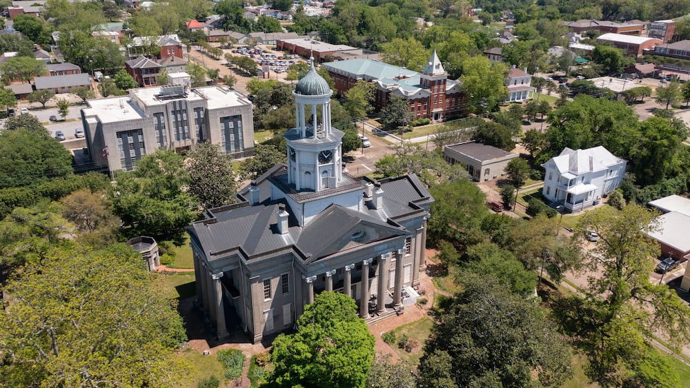A large historic building with a clock tower, surrounded by trees and other buildings.