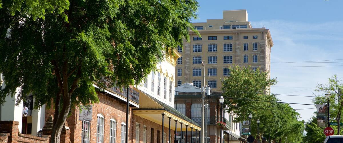A street lined with historic buildings, a car driving down the road, and a large building in the background.