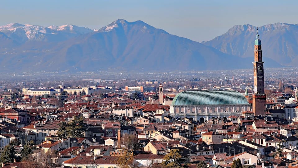 A cityscape with a prominent mosque, a cathedral, and snow-capped mountains in the background.