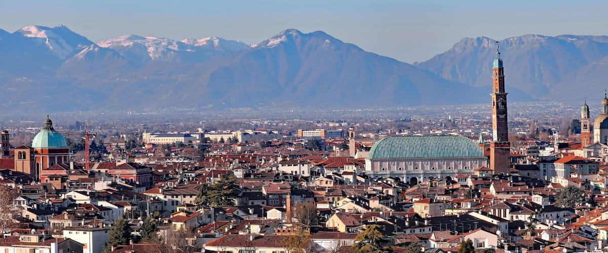 A cityscape with a prominent mosque, a cathedral, and snow-capped mountains in the background.