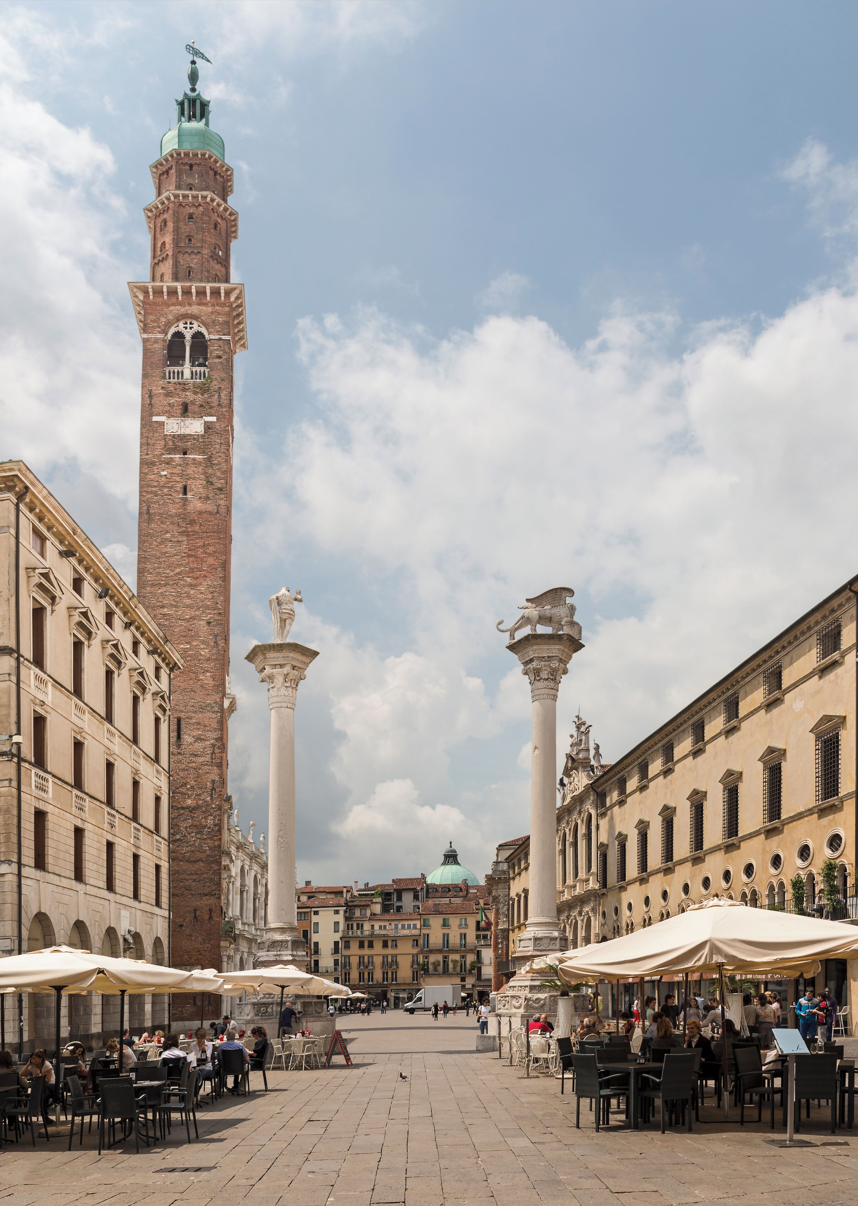 A historic square with a prominent tower, columns, and outdoor cafes.