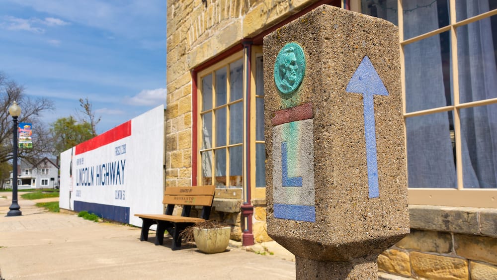 A stone marker with an arrow, a bench, a planter, and a building with a large sign.