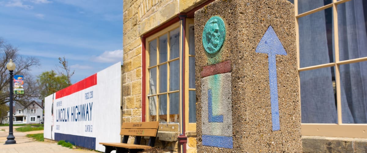 A stone marker with an arrow, a bench, a planter, and a building with a large sign.