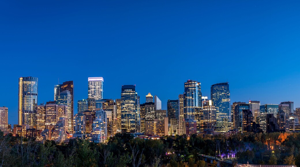 Un horizonte urbano al anochecer con edificios iluminados y un río en primer plano.