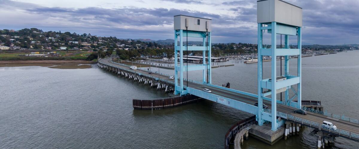 A large blue bridge spanning a river with a cityscape in the background.