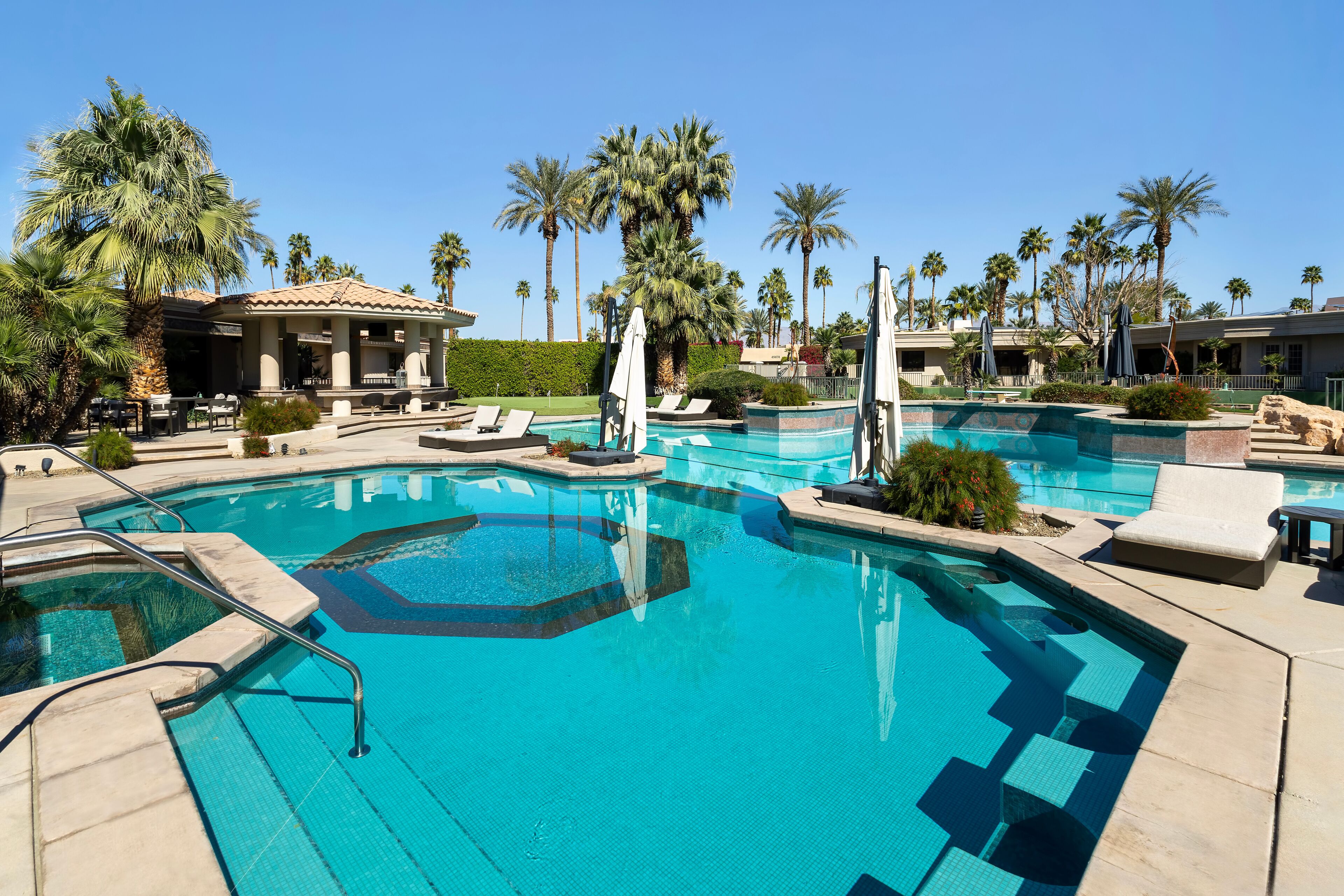 A pool with lounge chairs and palm trees.