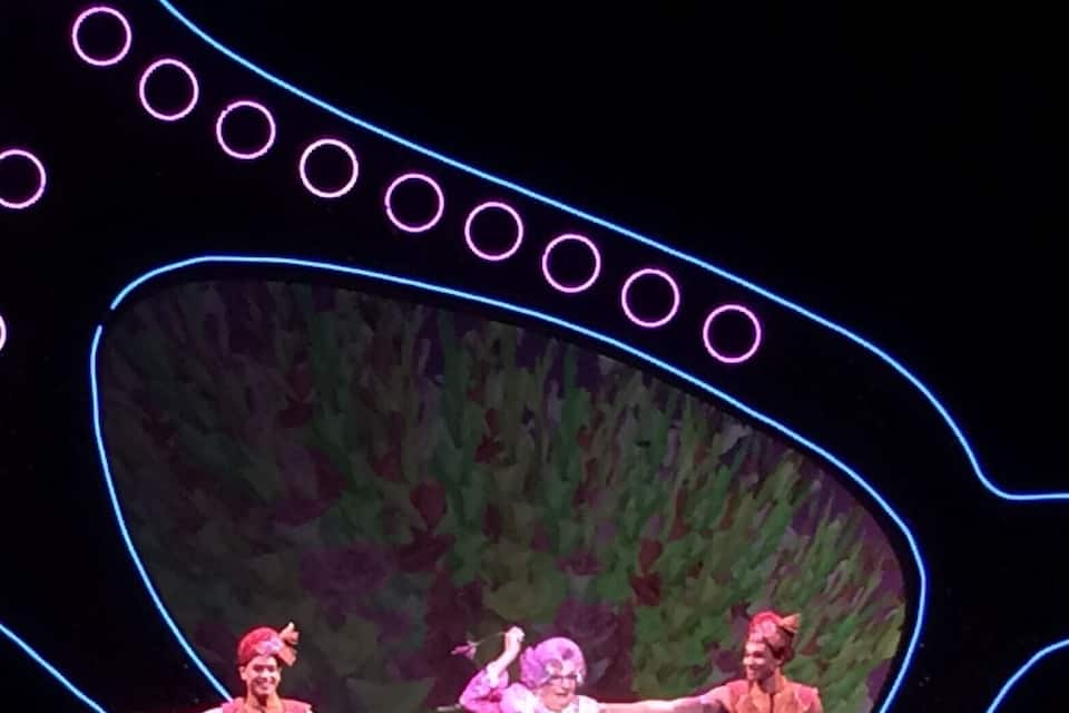 Drie artiesten op het podium, met een groot scherm waarop een beeld van een boom staat.