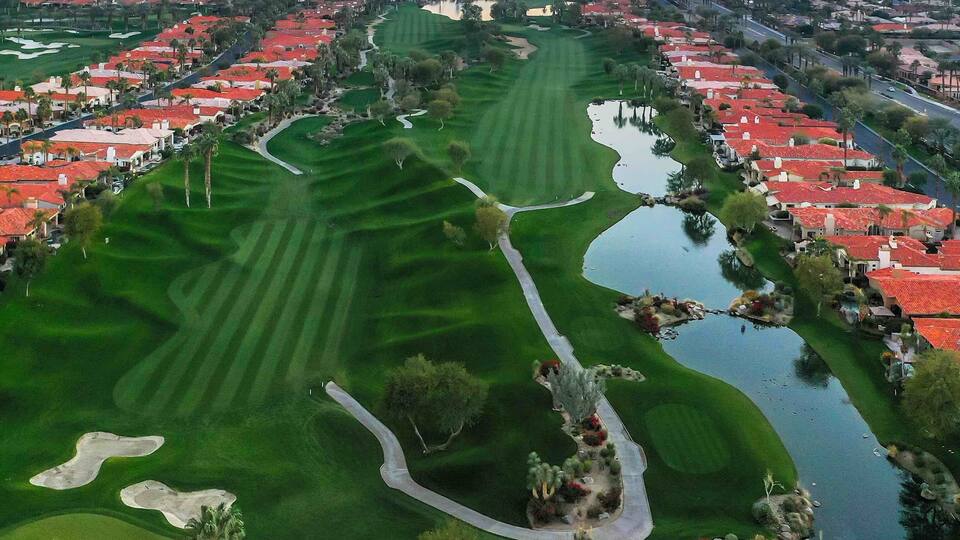 A golf course with water hazards, sand bunkers, and a backdrop of mountains.