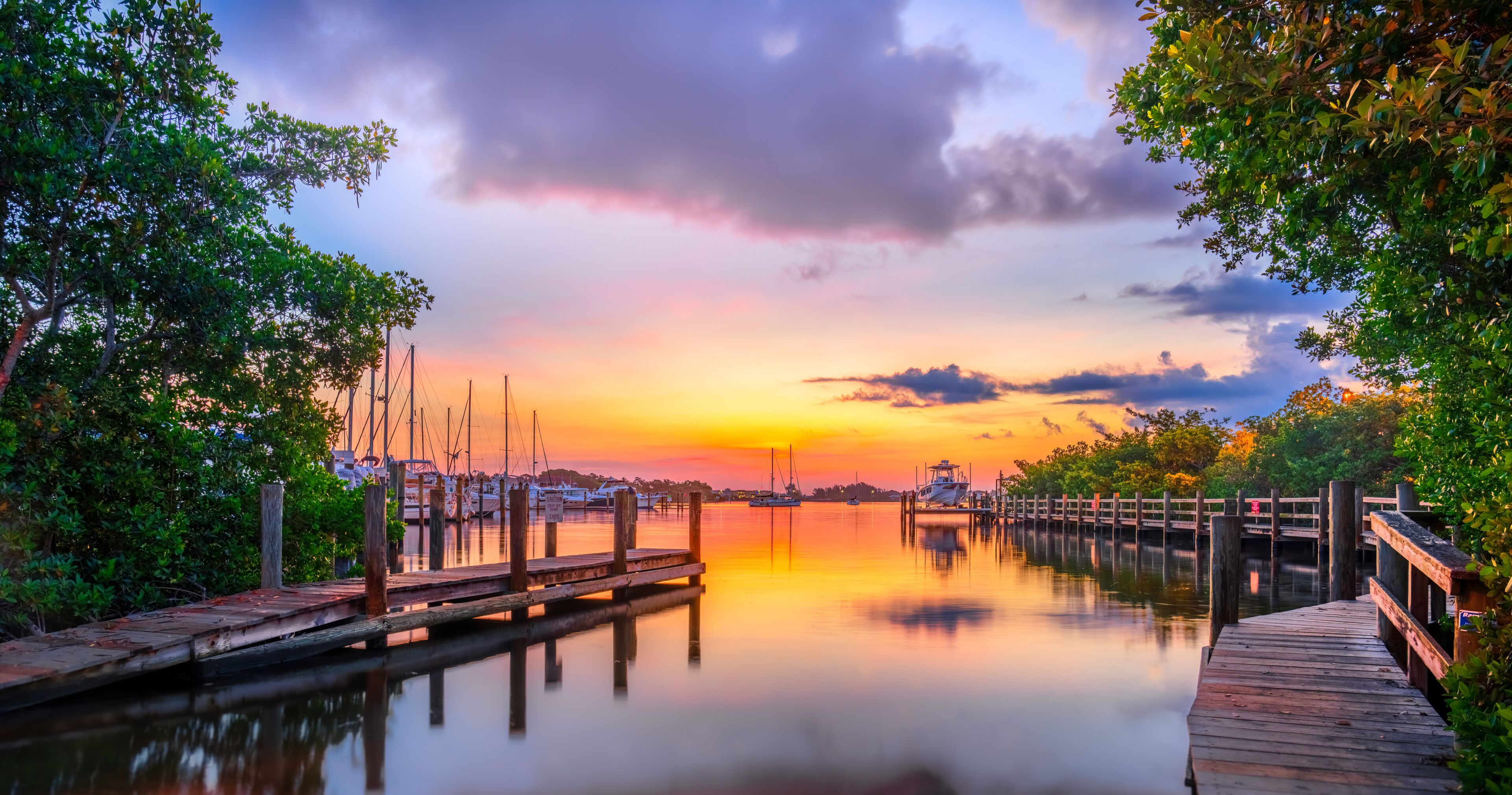 A calm waterfront with a wooden dock, boats, and a sunset sky.