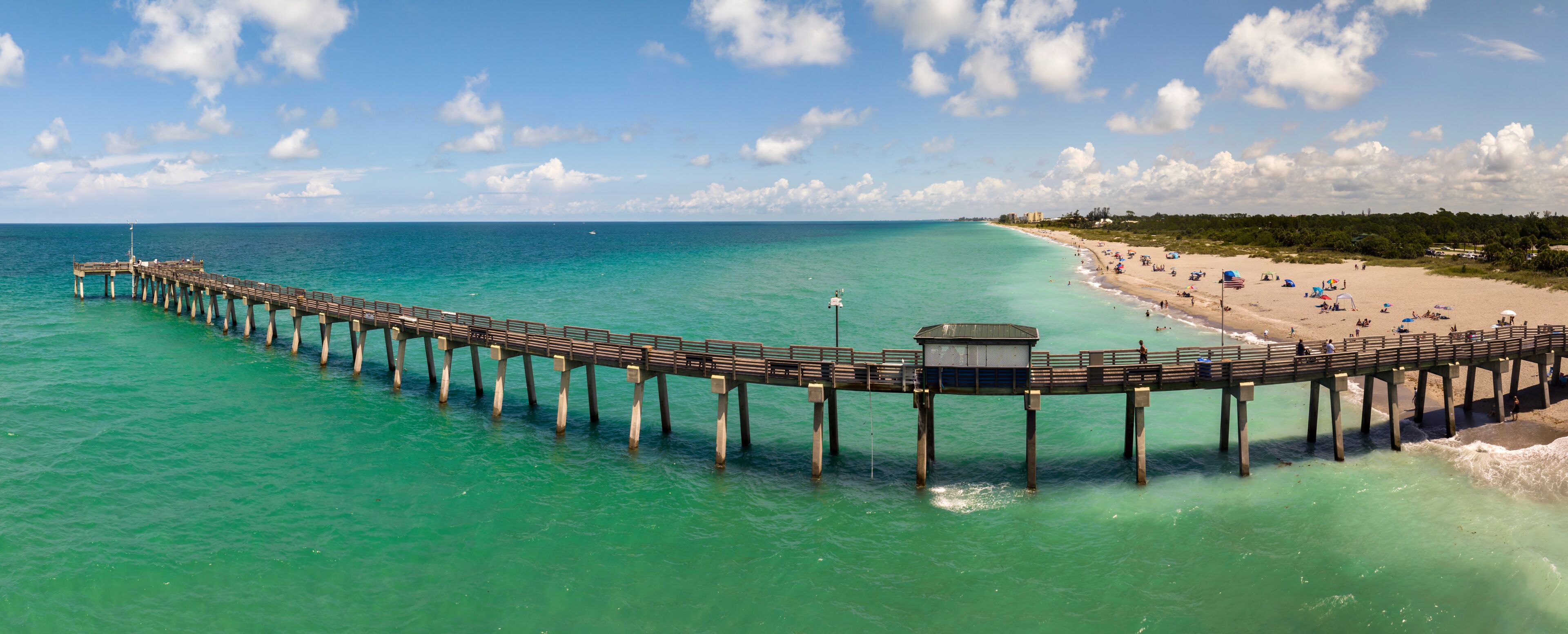 A pier extending into turquoise waters with a beach and palm trees in the background.